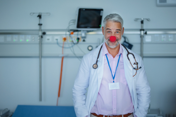 Portrait of happy doctor with clown red nose in hospital room.