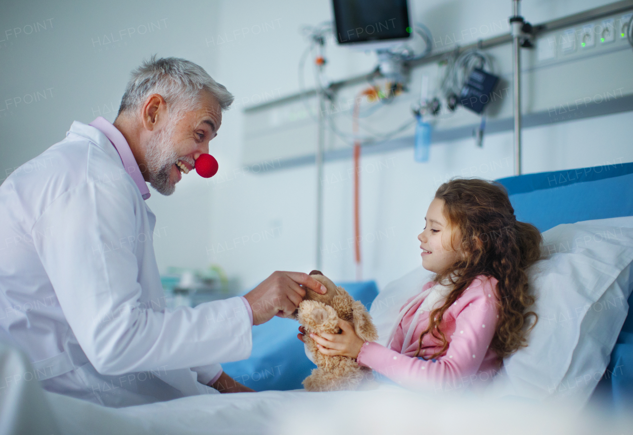 Happy doctor with clown red nose taking care and playing with a little girl.