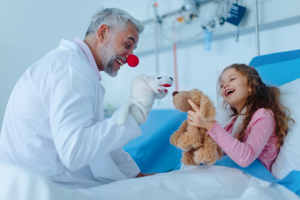 Happy doctor with clown red nose taking care and playing with a little girl.