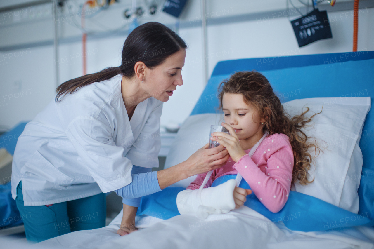 Young nurse giving glass of water to the little girl.