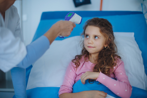 Nurse measuring body temperature to little girl lying in a hospital.