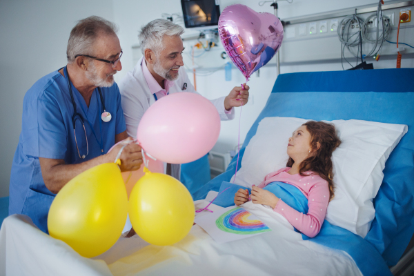 Happy doctors celebrating birthday with little girl in a hospital room.