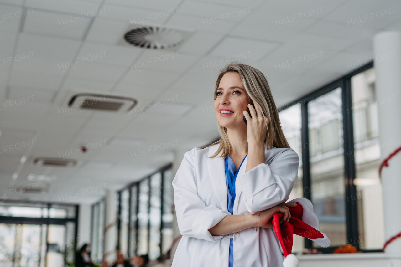 Portrait of beautiful female doctor with christmas hat in hand phone calling. Working in hospital on the Christmas day, Christmas Eve. Female doctor working a Christmas shift and can't be with her family.