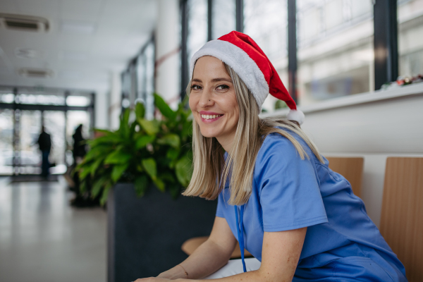 Beautiful nurse with christmas hat sitting in hospital waiting room, corridor. Obstetrics nurse working in hospital on the Christmas day, Christmas Eve. Female doctor working a Christmas shift and can't be with her family.