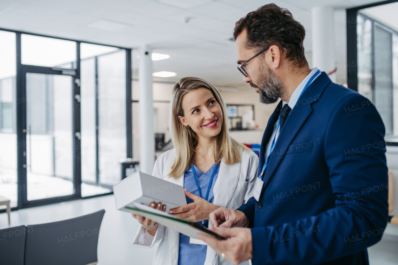 Portrait of pharmaceutical sales representative talking with doctor in medical building. Ambitious male sales representative in suit presenting new medication.