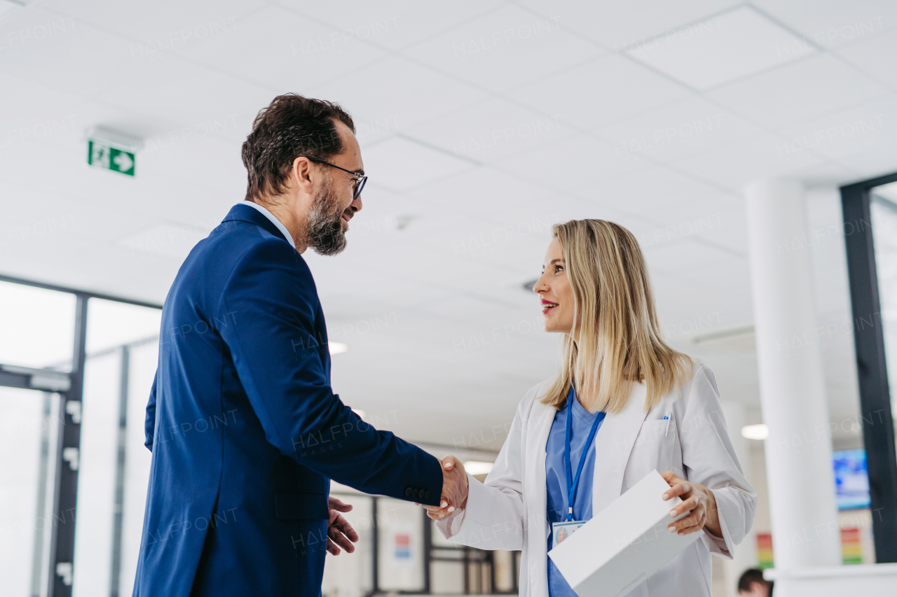 Portrait of pharmaceutical sales representative talking with doctor in medical building. Ambitious male sales representative in suit presenting new medication on tablet.