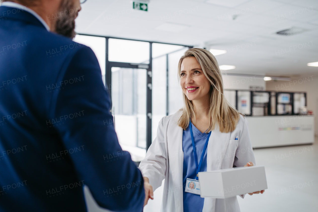 Portrait of pharmaceutical sales representative talking with doctor in medical building. Ambitious male sales representative in suit presenting new medication.