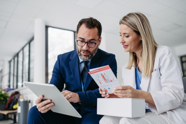 Portrait of pharmaceutical sales representative talking with doctor in medical building. Ambitious male sales representative in suit presenting new medication.