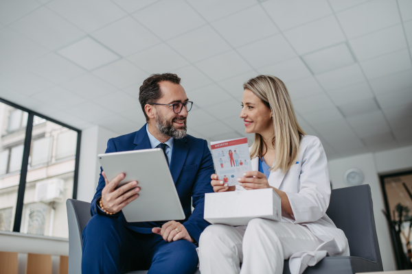 Portrait of pharmaceutical sales representative talking with doctor in medical building. Ambitious male sales representative in suit presenting new medication.