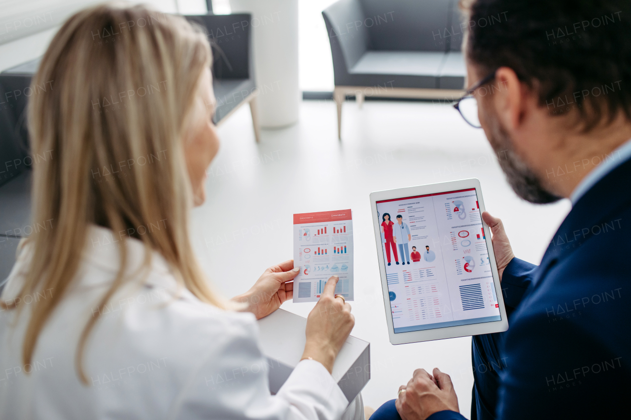 Rear view of pharmaceutical sales representative talking with doctor in medical building. Ambitious male sales representative in suit presenting new medication.