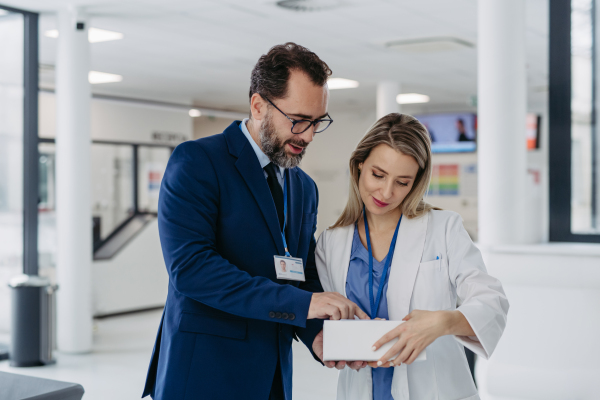 Portrait of pharmaceutical sales representative talking with doctor in medical building. Ambitious male sales representative in suit presenting new medication.