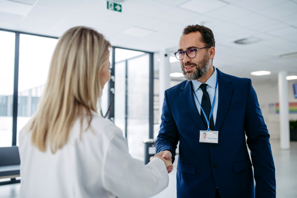 Portrait of pharmaceutical sales representative talking with doctor in medical building, clinic lobby. Ambitious male sales representative in suit shaking hand with female doctor.