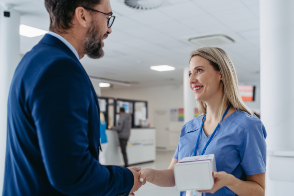 Portrait of pharmaceutical sales representative talking with doctor in medical building. Ambitious male sales representative in suit presenting new medication on tablet.