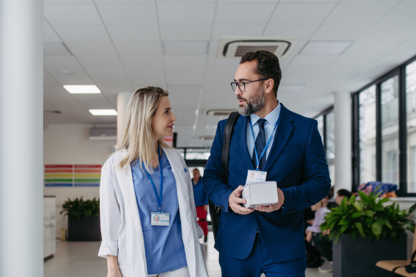 Portrait of pharmaceutical sales representative talking with doctor in medical building. Ambitious male sales representative in suit presenting new medication.