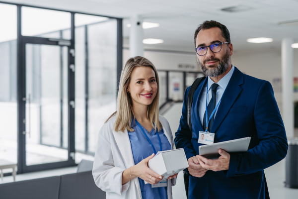 Portrait of pharmaceutical sales representative talking with doctor in medical building. Ambitious male sales representative in suit presenting new medication on tablet.