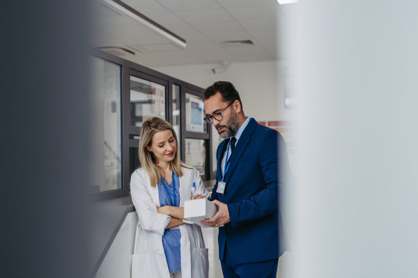 Portrait of pharmaceutical sales representative talking with doctor in medical building. Ambitious male sales representative in suit presenting new medication on tablet.