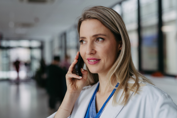 Portrait of beautiful ER doctor in hospital phone calling. Remote consultations with patient, telemedicine.