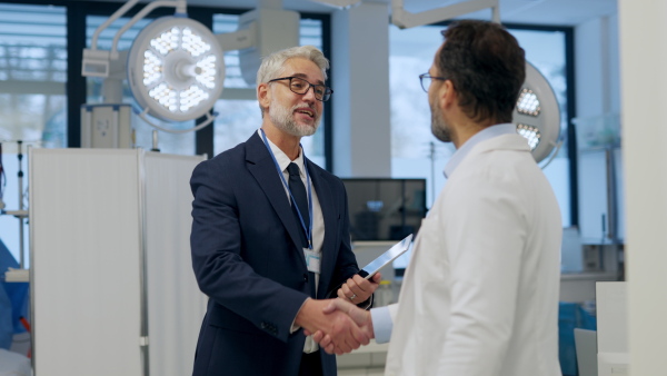 Portrait of pharmaceutical sales representative standing in doctor office, shaking hands. Hospital director, manager of private medical clinic greeting new doctor. Generous donor, giving donation to hospital.