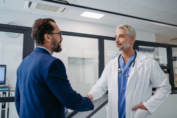 Portrait of pharmaceutical sales representative standing in doctor office, shaking hands. Hospital director, manager of private medical clinic greeting new doctor. Generous donor, giving donation to hospital.