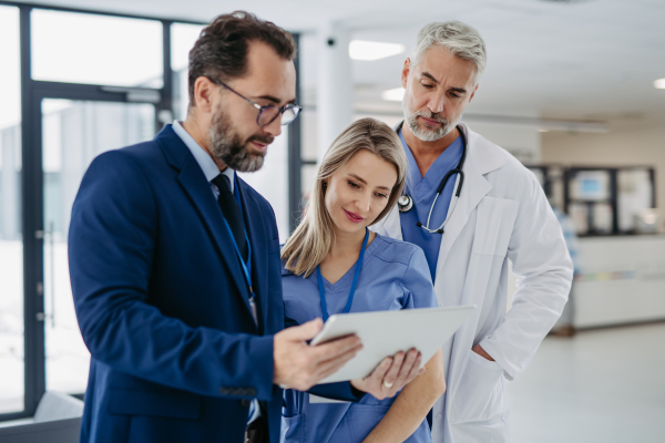 Pharmaceutical sales representative talking with doctors in medical building, presenting new medication on tablet. Hospital director or manager in modern clinic with the doctor and nurse.