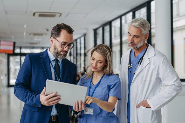 Pharmaceutical sales representative talking with doctors in medical building, presenting new product on tablet. Hospital director, manager in private medical clinic handshaking with doctors.