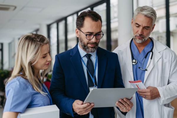 Pharmaceutical sales representative presenting new medication to doctors in medical building, showing on tablet. Hospital director of private medical clinic talking with doctors. Generous donor, giving donation to hospital.