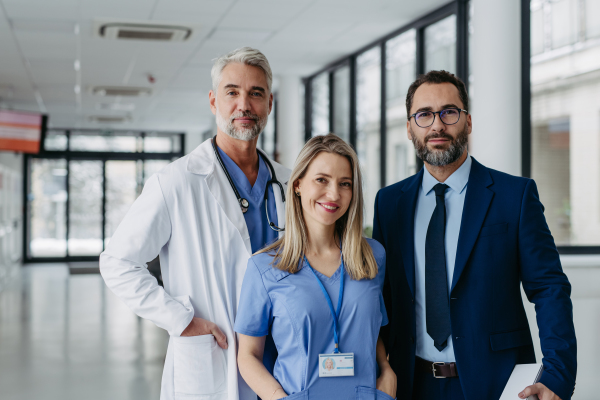 Portrait of female doctor standing in front of male colleagues. Beautiful nurse in uniform, standing in modern private clinic, looking at camera.