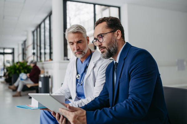 Pharmaceutical sales representative talking with doctor in medical building. Ambitious male sales representative in suit presenting new medication.