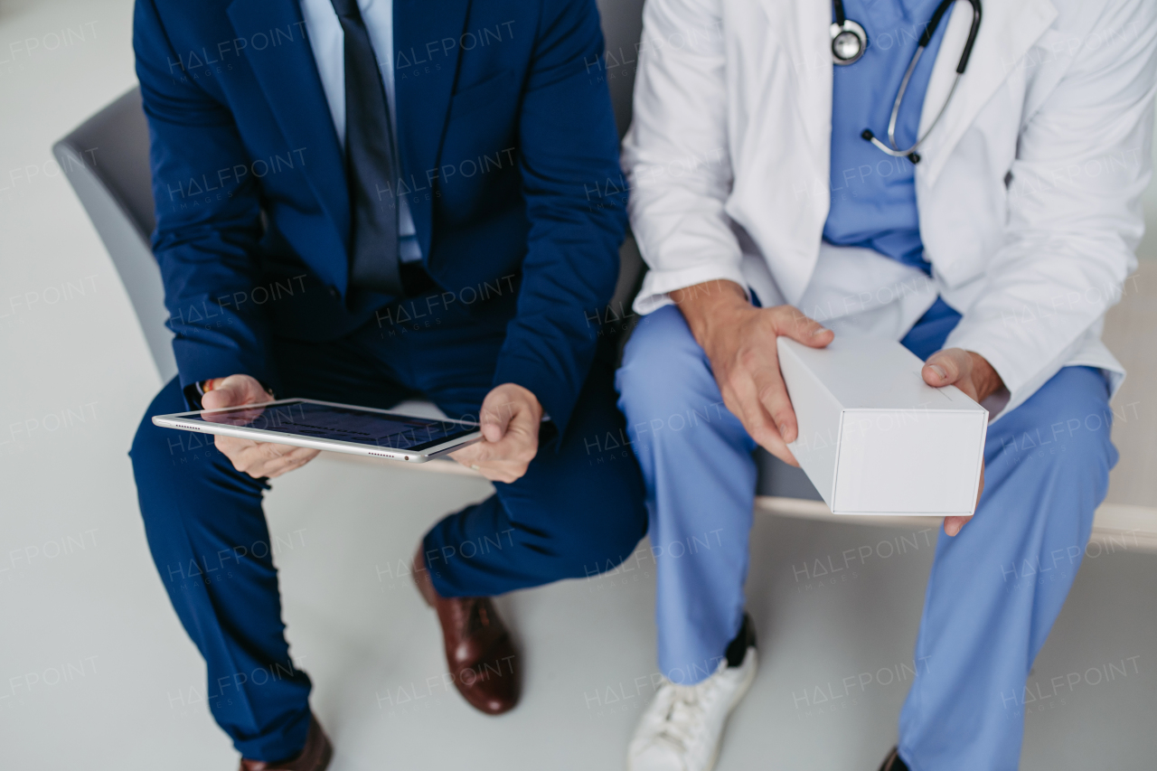 Close up on legs of pharmaceutical sales representative talking with doctor in medical building, presenting new medication on tablet. Hospital director or manager in modern clinic with surgeon.