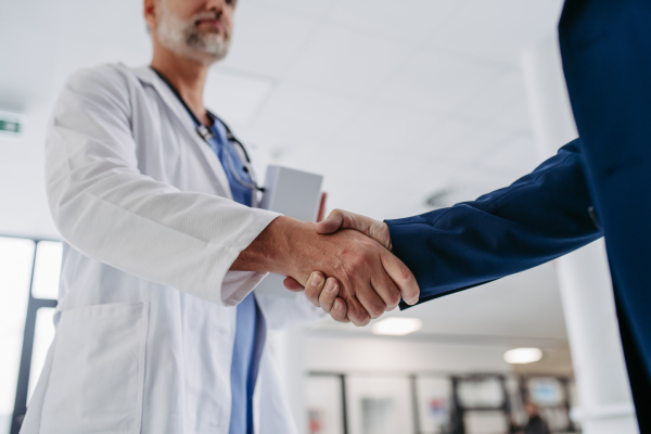 Close up of pharmaceutical sales representative standing in doctor office, shaking hands. Hospital director, manager of private medical clinic greeting new doctor. Generous donor, giving donation to hospital.