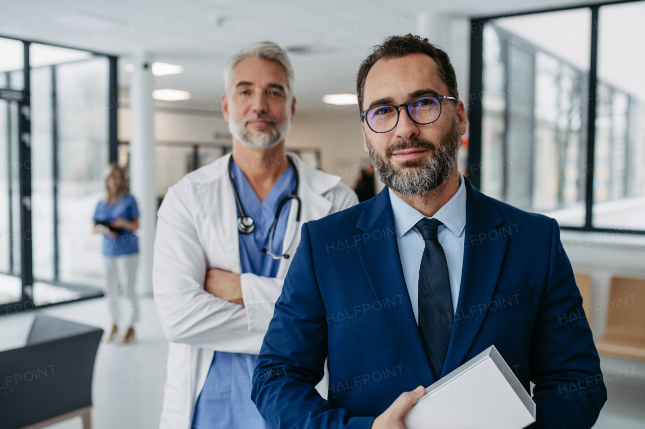 Portrait of pharmaceutical sales representative standing in hospital corridor. Hospital director, manager of private medical clinic in hospital lobby. Doctor standing behind him.