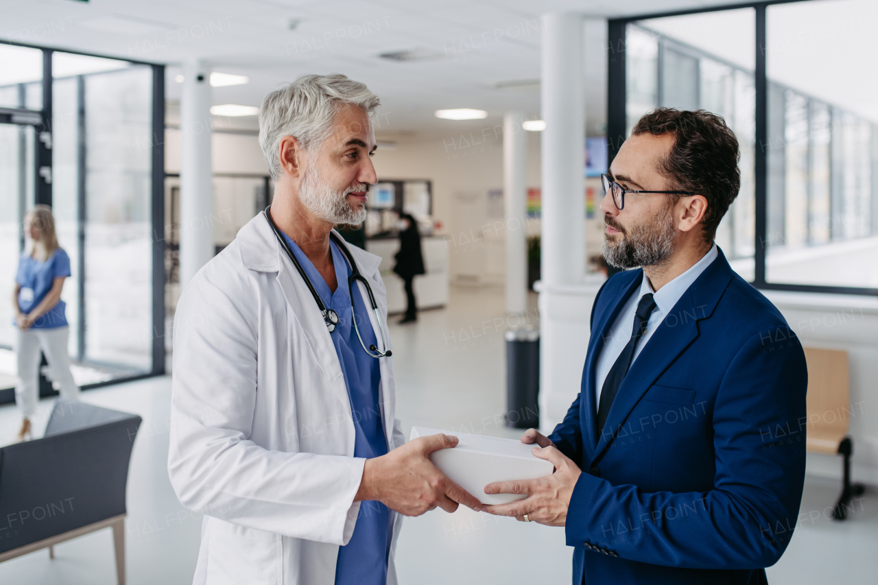 Pharmaceutical sales representative presenting new medication to doctor in medical building, holding and handing box with medication, drugs samples to doctor.