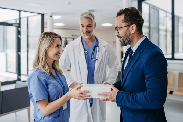 Pharmaceutical sales representative presenting new product to doctors in holding box with pills. Presenting new pharmaceutical product, drugs, medication.Hospital director, manager in private medical clinic showing something on tablet.