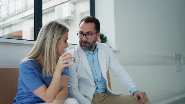 Handsome doctor and nurse taking a break during work shift at hospital, drinking waterand talking in hospital lobby.