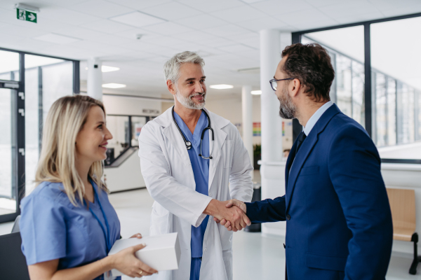 Pharmaceutical sales representative talking with doctors in medical building, shaking hands. Drug rep presenting new pharmaceutical product, drug. Hospital director, manager in private medical clinic handshaking with doctors.