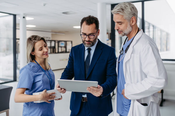 Pharmaceutical sales representative presenting new medication to doctors in medical building, showing on tablet. Hospital director of private medical clinic talking with doctors. Generous donor, giving donation to hospital.