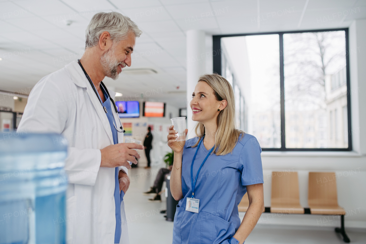 Handsome doctor and nurse taking a break during work shift at hospital, drinking water from water dispenser in hospital lobby, talking.