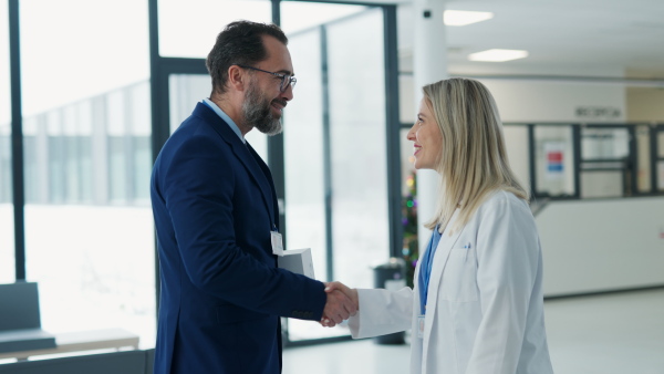 Portrait of pharmaceutical sales representative talking with doctor in medical building. Ambitious male sales representative in suit presenting new medication on tablet.