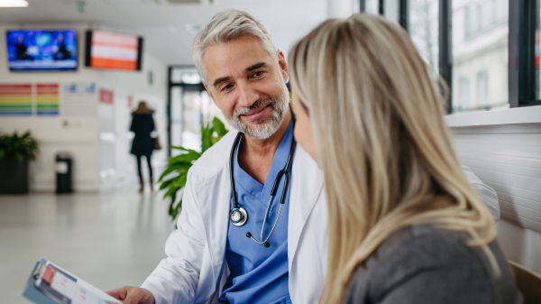 Pharmaceutical sales representative talking with doctor in modern clinic. Ambitious female medical rep presenting new medication. Female hospital director with doctor. Banner with copy space.