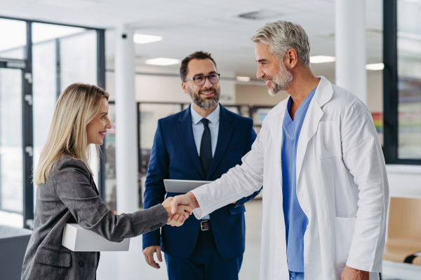 Pharmaceutical sales representatives meeting doctor in medical building, shaking hands. Hospital director and manager talking with head physician in modern clinic, hospital. Generous donor, giving donation to hospital.