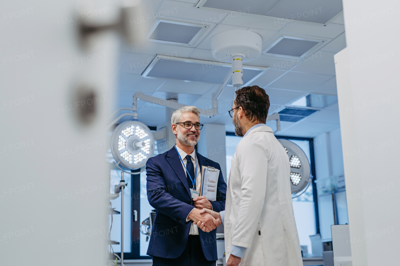 Portrait of pharmaceutical sales representative standing in doctor office, shaking hands. Hospital director, manager of private medical clinic greeting new doctor. Generous donor, giving donation to hospital. Through door.