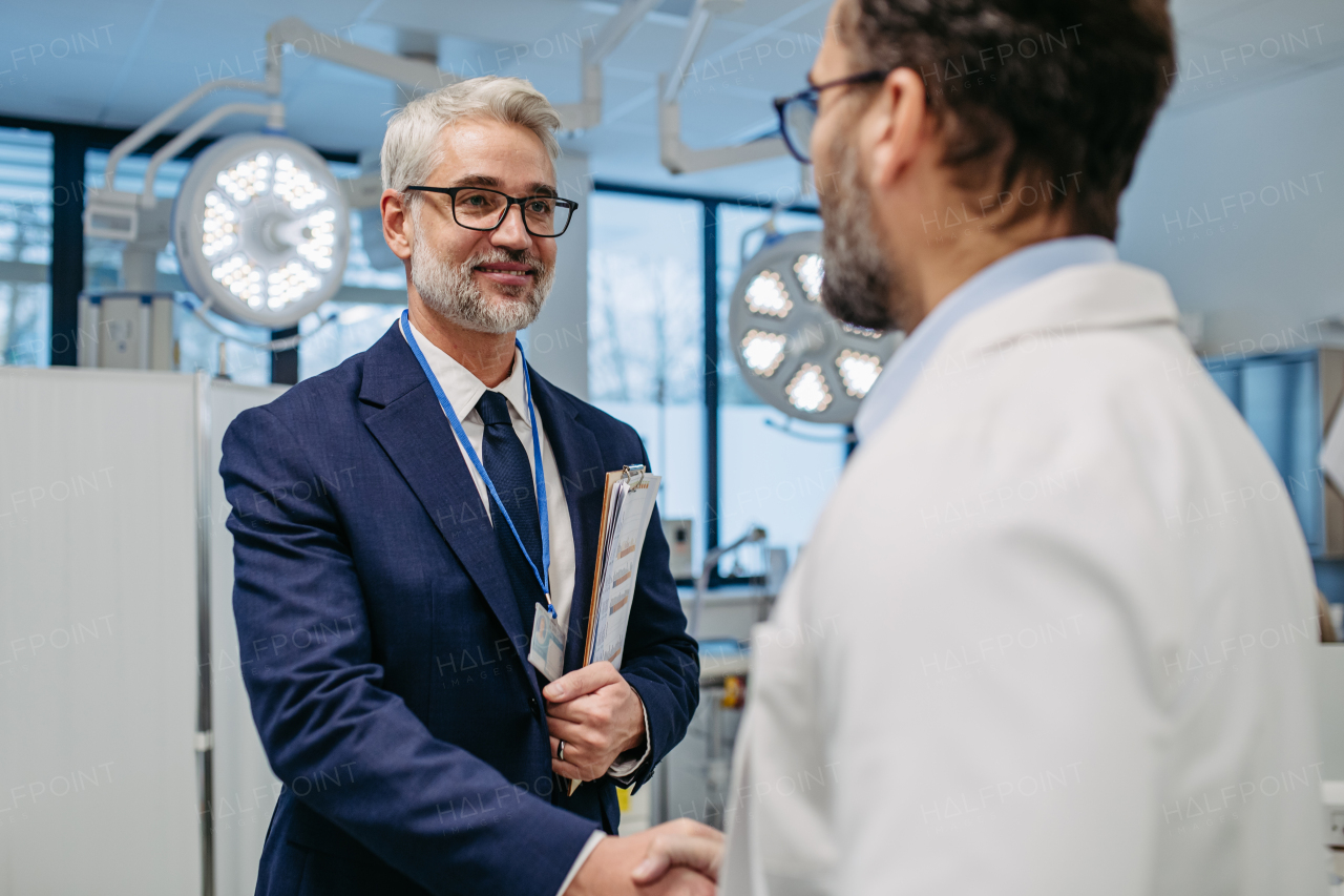 Portrait of pharmaceutical sales representative standing in doctor office, shaking hands. Hospital director, manager of private medical clinic greeting new doctor. Generous donor, giving donation to hospital.