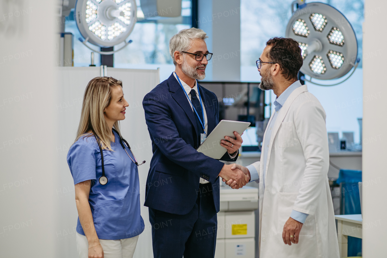 Portrait of pharmaceutical sales representative standing in doctor office, shaking hands. Hospital director, manager of private medical clinic greeting new doctors. Generous donor, giving donation to hospital. Through door.