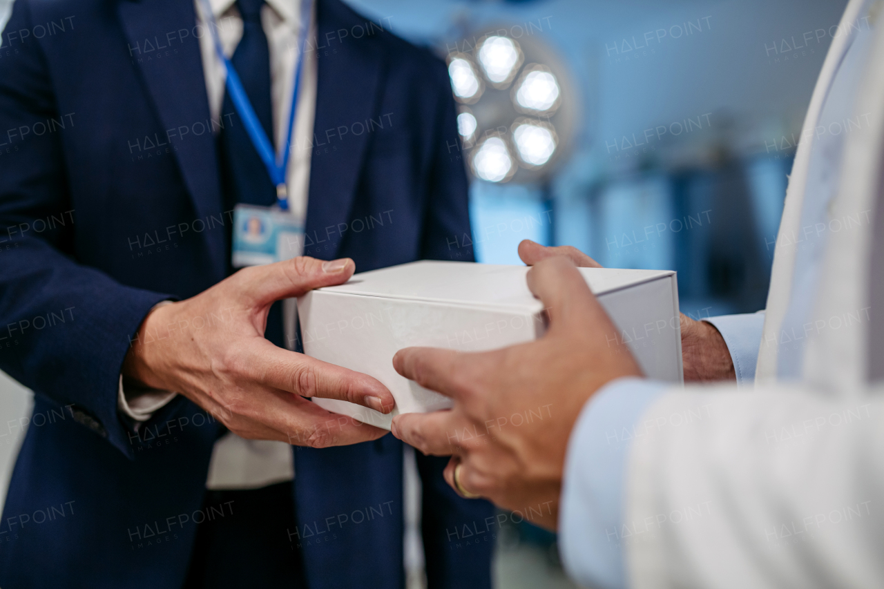 Pharmaceutical sales representative presenting new medication to doctor in medical building, holding and handing box with medication, drugs samples to doctor.