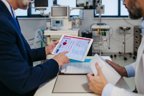 Pharmaceutical sales representative presenting new medication to doctor in medical building, holding box with medication, drugs samples.