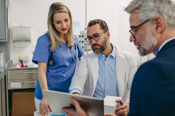 Pharmaceutical sales representative talking with doctors in medical building, presenting new product on tablet. Hospital director, manager in private medical clinic handshaking with doctors.