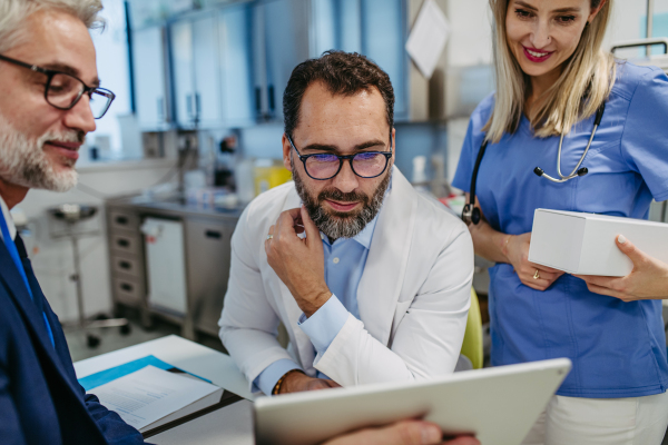 Pharmaceutical sales representative presenting new product to doctors in holding tablet. Presenting new pharmaceutical product, drugs, medication.Hospital director, manager in private medical clinic showing something on tablet.