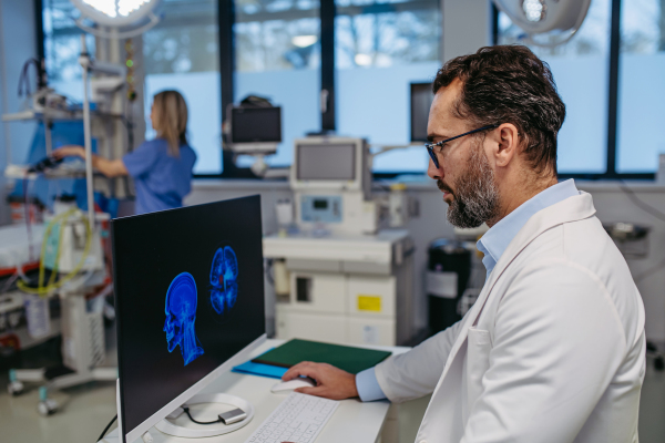 Side view of ER doctor in hospital working in emergency room. Healthcare worker looking at MRI scan on medical computer in emergency room.