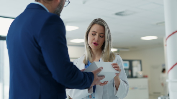 Portrait of pharmaceutical sales representative talking with doctor in medical building. Ambitious male sales representative in suit presenting new medication on tablet.