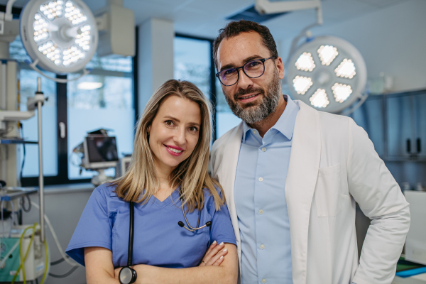 Portrait of confident doctor and nurse standing in examination room. Healthcare workers in modern private clinic, looking at camera and smiling.